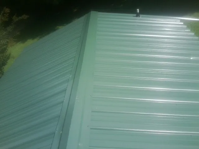 New green metal panels meeting at the ridge of a roof — Flat Roof Repair work by our crew in Nauvoo