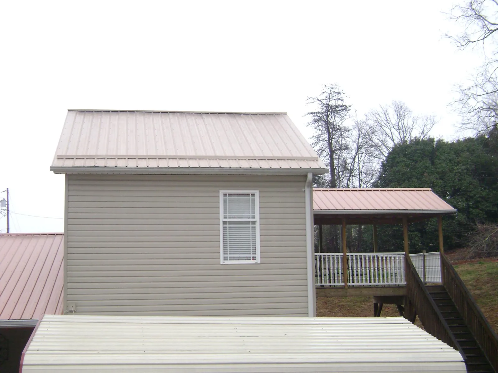 Tan metal roofs on a two story addition and attached porch, from a Roof Replacement job in Nauvoo
